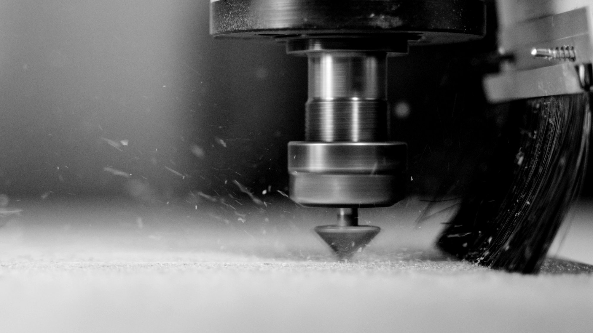 CNC router cutting a wood panel, close-up on the bit and sawdust